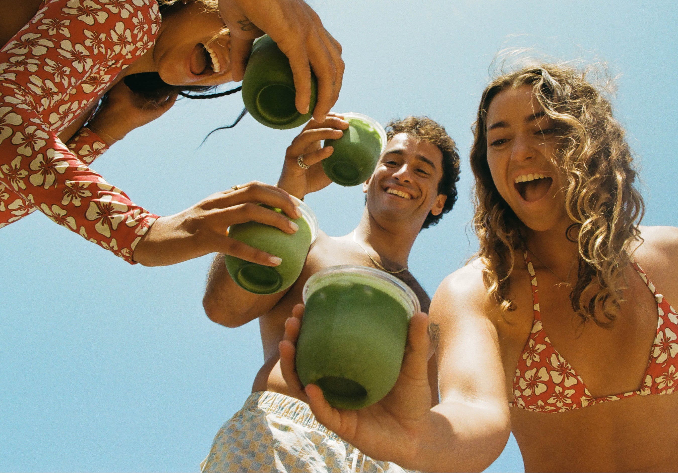 Three people enjoying green matcha lattes against a clear blue sky.